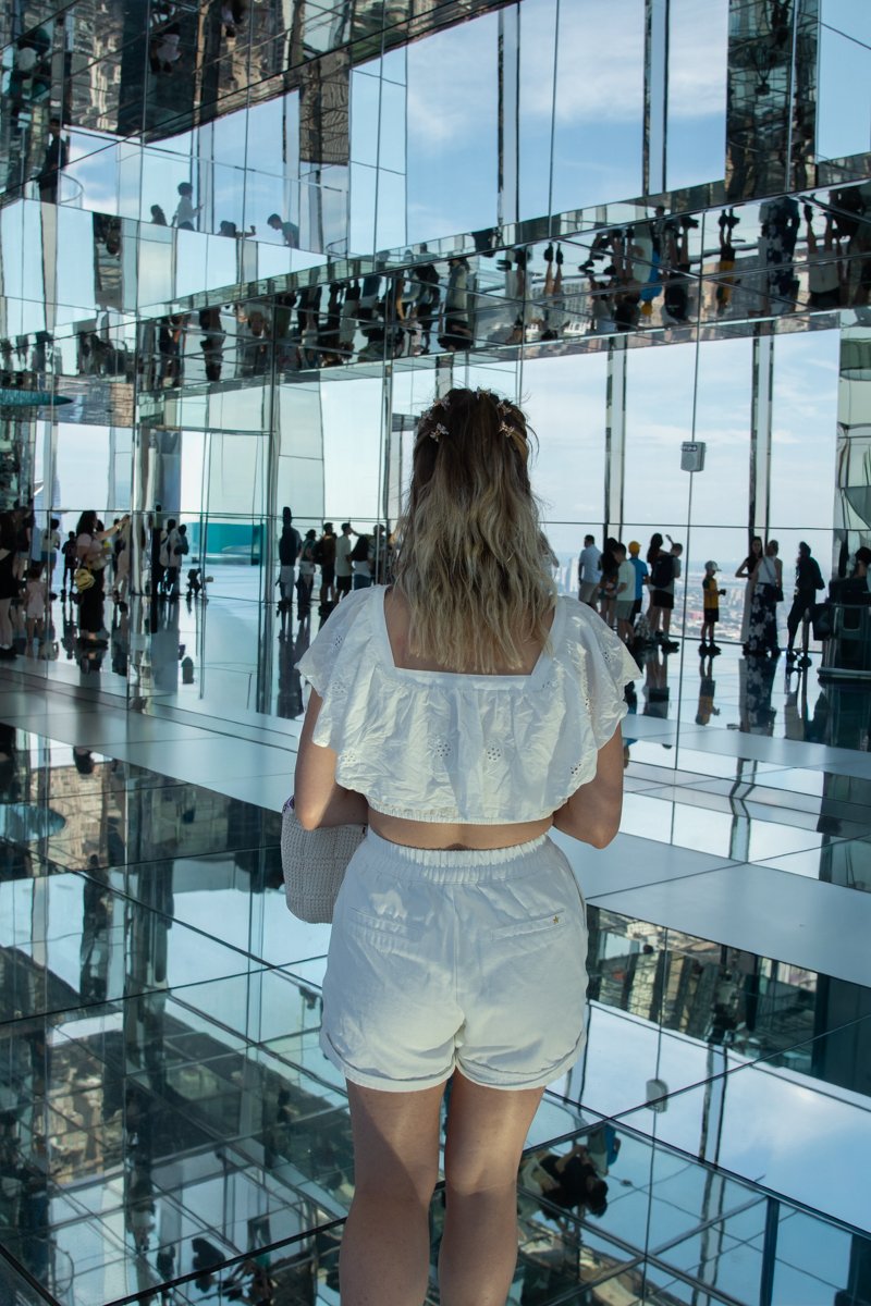 Personne qui marche à l'étage 91 au milieu des vitres et miroirs