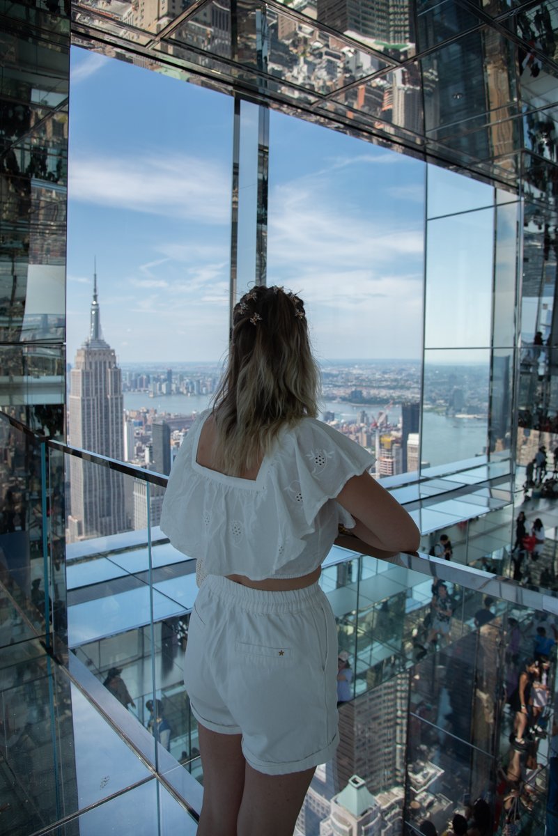 Femme qui se tient sur une rambarde de l'étage 91, avec l'Empire State Building en arrière-plan